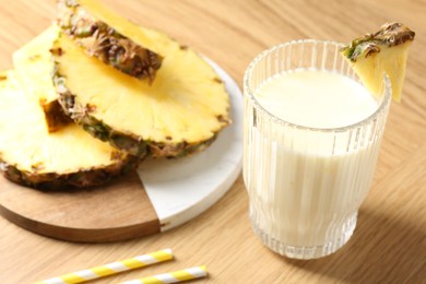 Photo of Tasty pineapple smoothie in glass and fresh fruit on wooden table, closeup