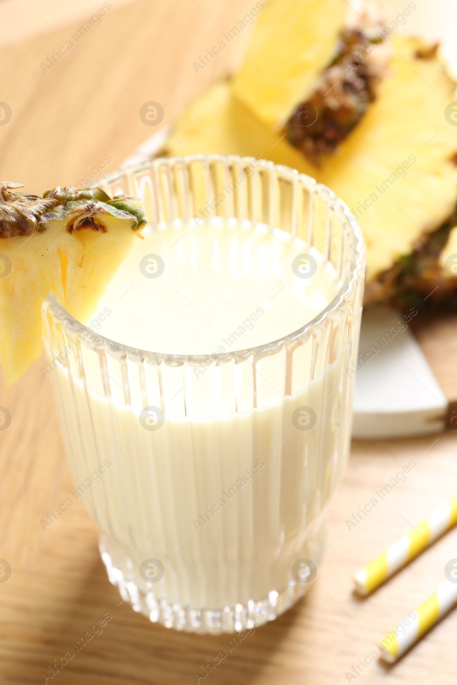 Photo of Tasty pineapple smoothie in glass and fresh fruit on wooden table, closeup