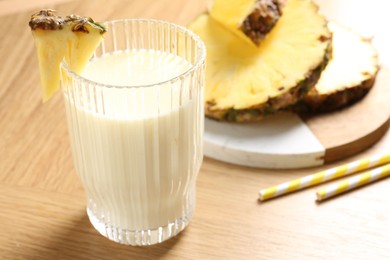 Photo of Tasty pineapple smoothie in glass and fresh fruit on wooden table, closeup