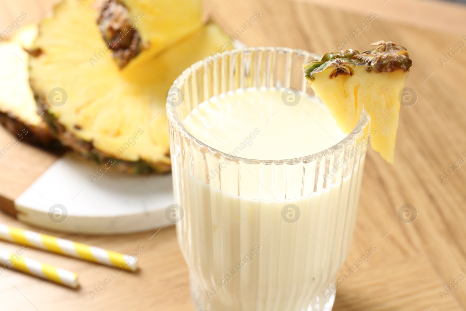 Photo of Tasty pineapple smoothie in glass and fresh fruit on wooden table, closeup