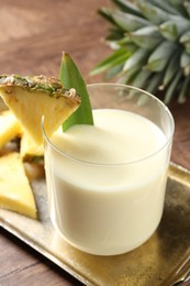 Photo of Tasty pineapple smoothie in glass and fresh fruit on wooden table, closeup