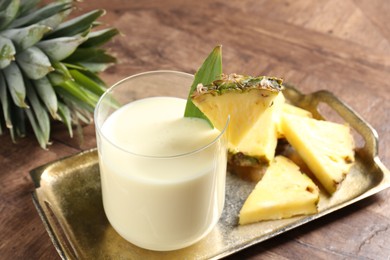 Photo of Tasty pineapple smoothie in glass and fresh fruit on wooden table, closeup