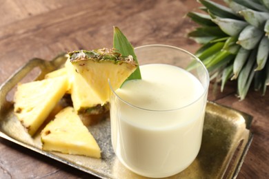 Photo of Tasty pineapple smoothie in glass and fresh fruit on wooden table, closeup