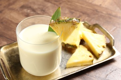 Photo of Tasty pineapple smoothie in glass and fresh fruit on wooden table, closeup