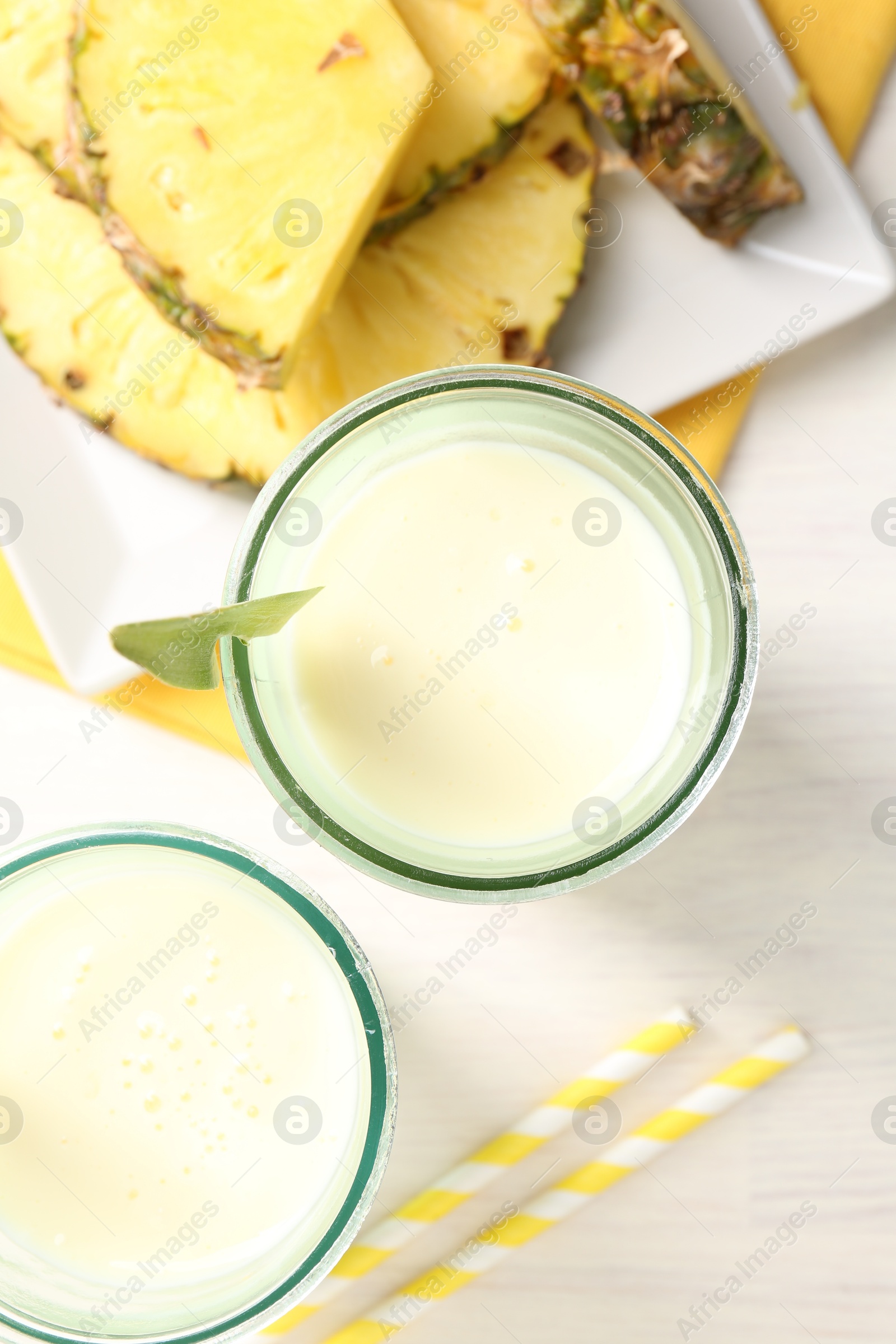 Photo of Tasty pineapple smoothie in glasses and fresh fruit on white wooden table, top view