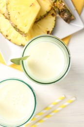 Photo of Tasty pineapple smoothie in glasses and fresh fruit on white wooden table, top view