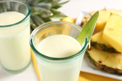 Photo of Tasty pineapple smoothie in glasses and fresh fruit on table, closeup