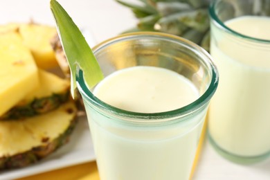 Photo of Tasty pineapple smoothie in glasses and fresh fruit on table, closeup