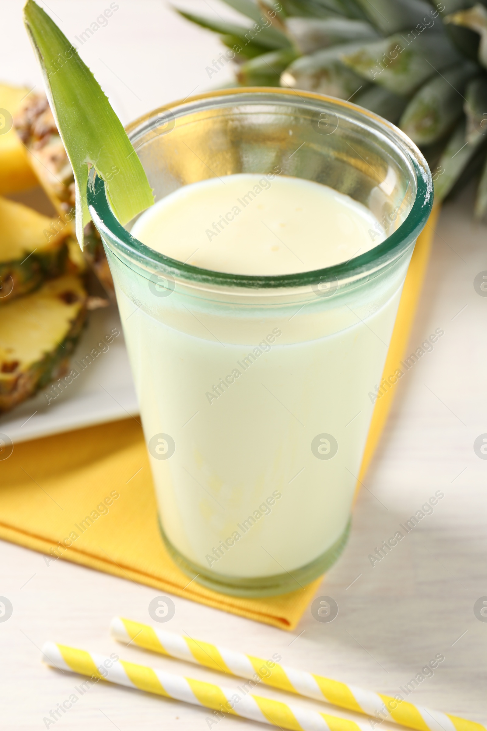 Photo of Tasty pineapple smoothie in glass and fresh fruit on white wooden table, closeup