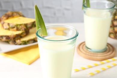 Photo of Tasty pineapple smoothie in glasses and fresh fruit on white table, closeup