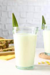 Photo of Tasty pineapple smoothie in glass on white wooden table