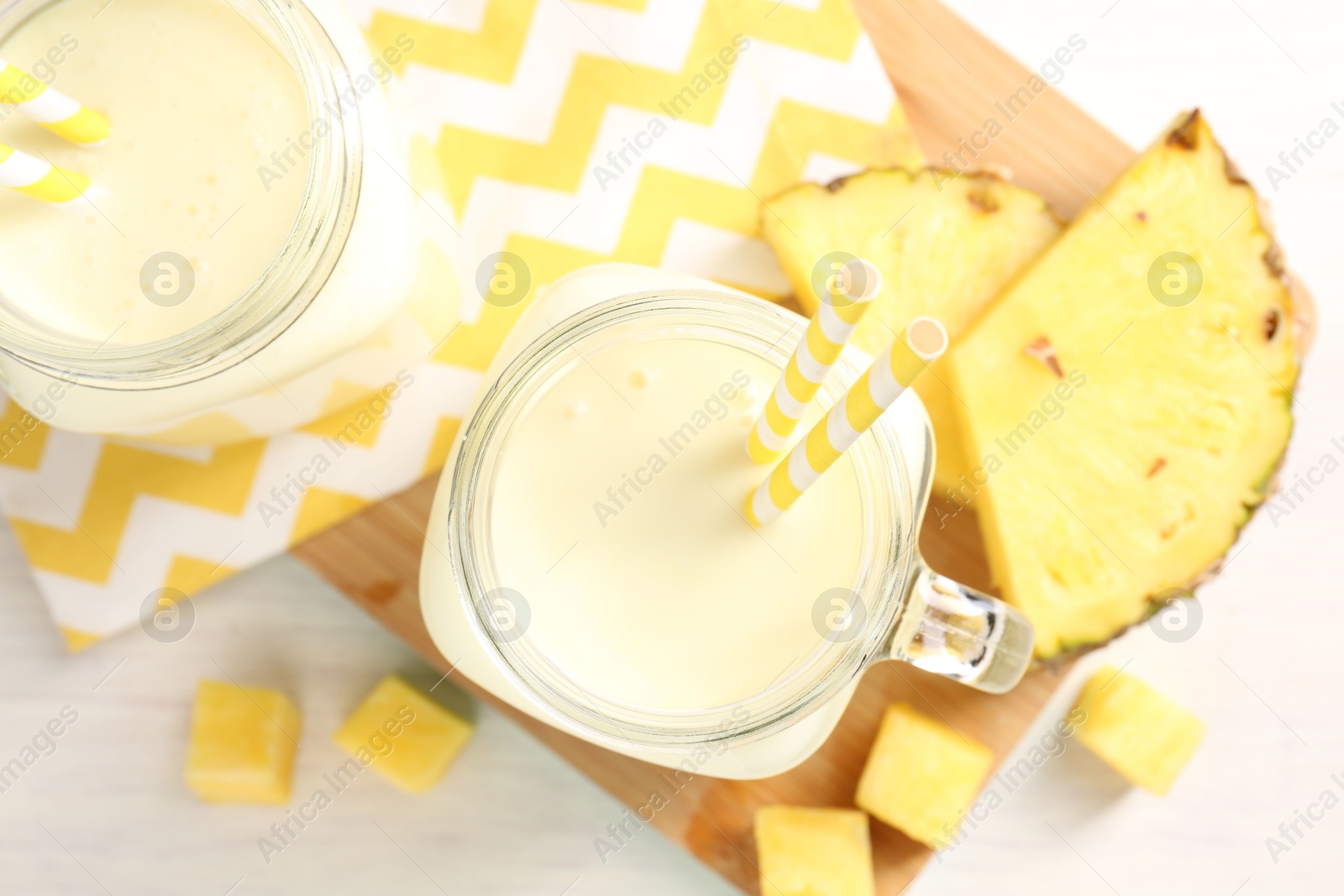 Photo of Tasty pineapple smoothie in mason jars and fresh fruit on white table, top view