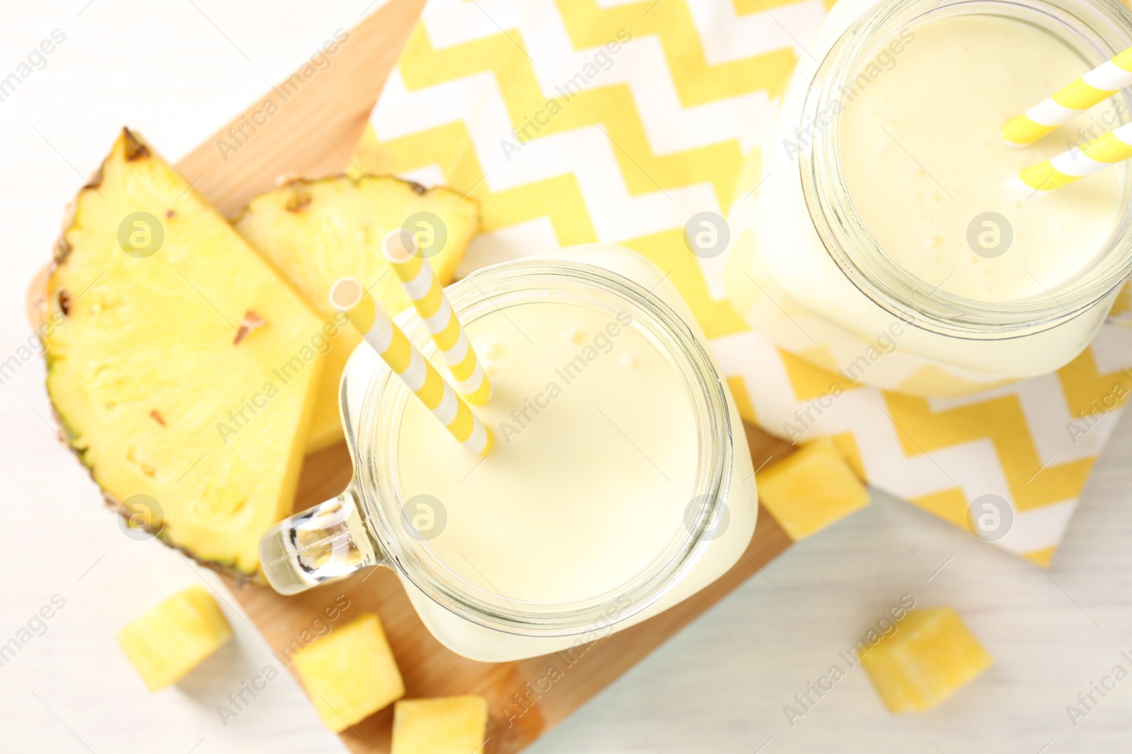 Photo of Tasty pineapple smoothie in mason jars and fresh fruit on white table, top view