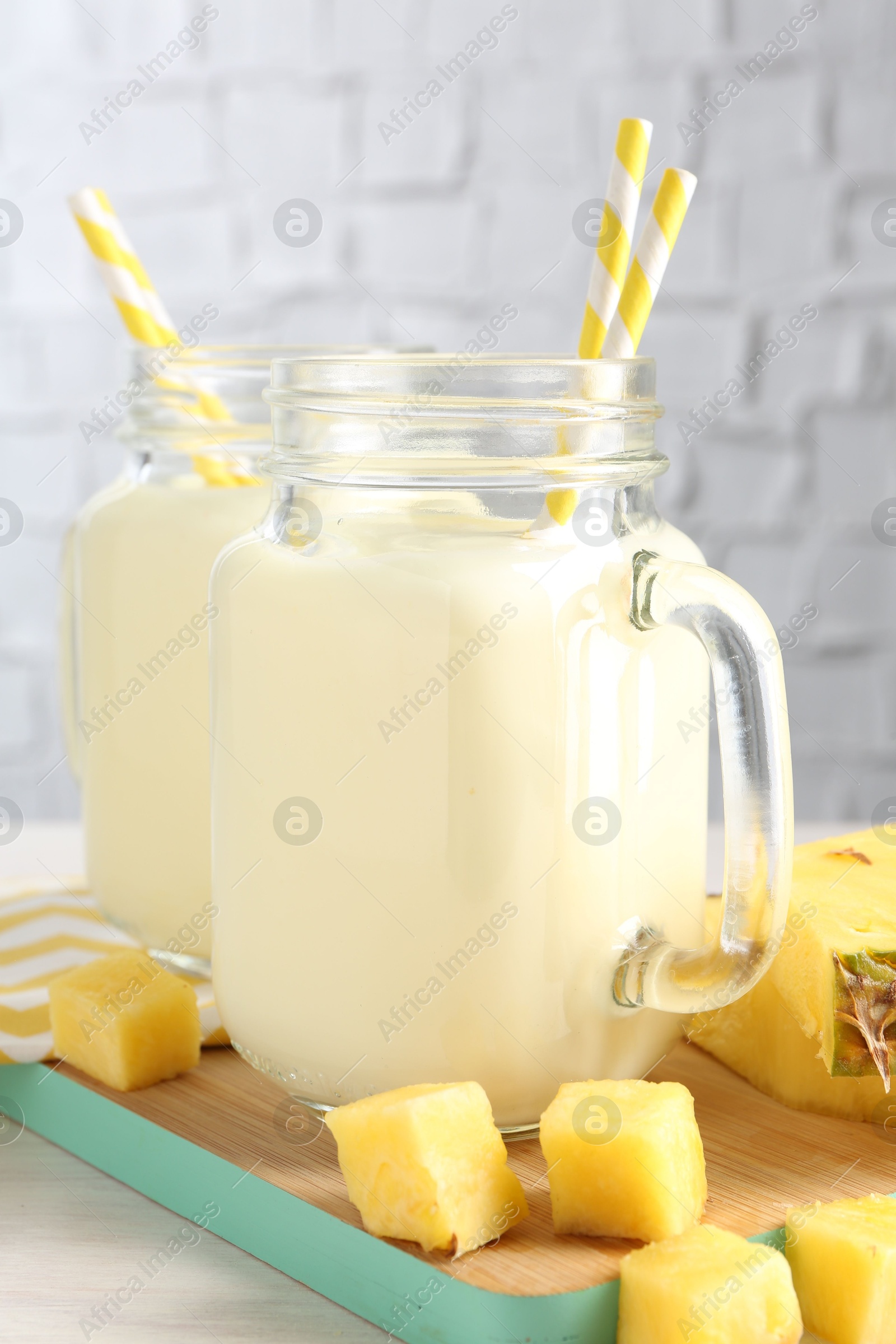 Photo of Tasty pineapple smoothie in mason jars and fresh fruit on table