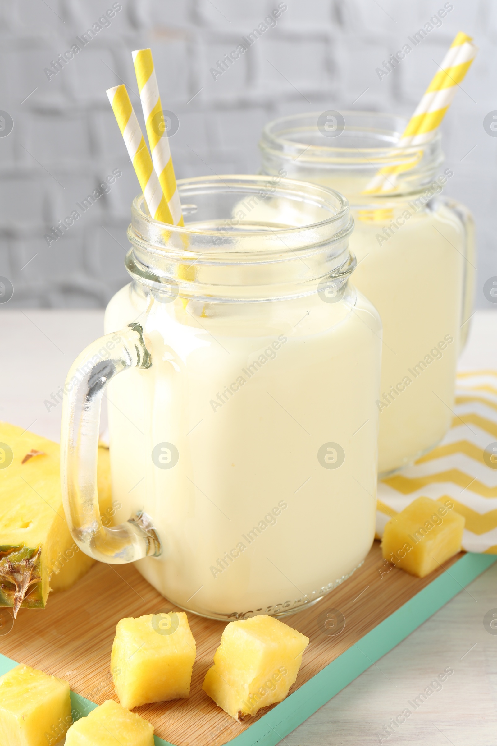 Photo of Tasty pineapple smoothie in mason jars and fresh fruit on table