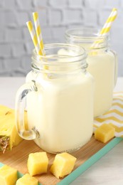 Photo of Tasty pineapple smoothie in mason jars and fresh fruit on table