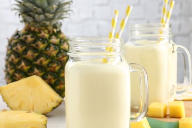 Photo of Tasty pineapple smoothie in mason jars and fresh fruit on table, closeup