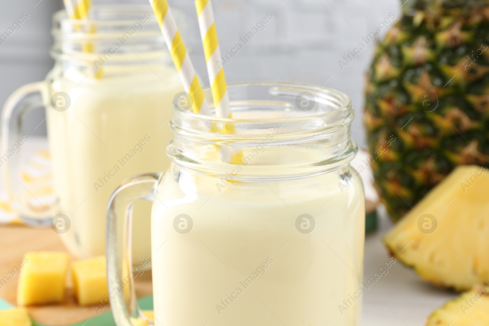 Photo of Tasty pineapple smoothie in mason jars and fresh fruit on table, closeup