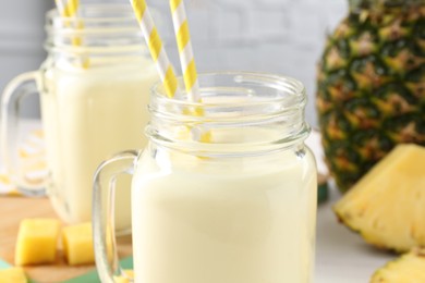 Photo of Tasty pineapple smoothie in mason jars and fresh fruit on table, closeup