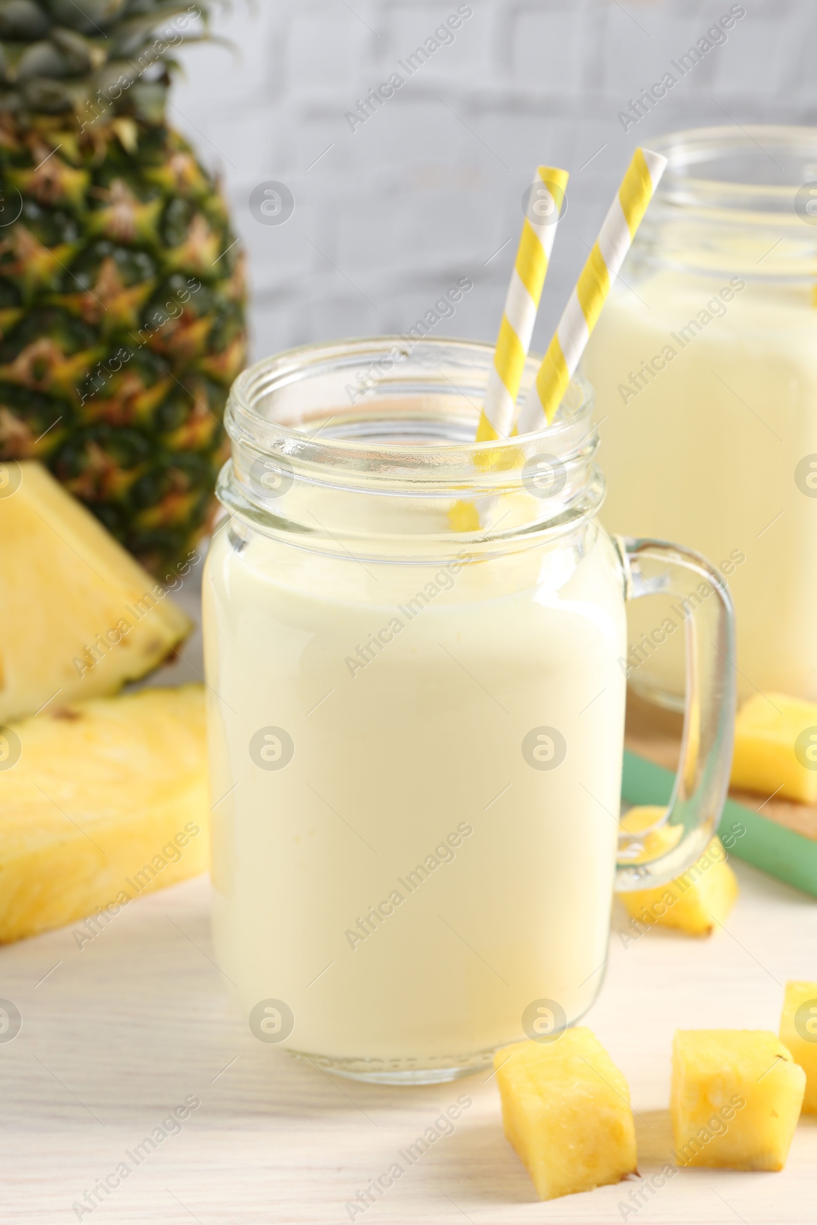 Photo of Tasty pineapple smoothie in mason jar and fresh fruit on white wooden table