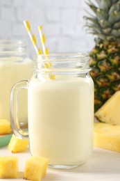 Photo of Tasty pineapple smoothie in mason jar and fresh fruit on white wooden table