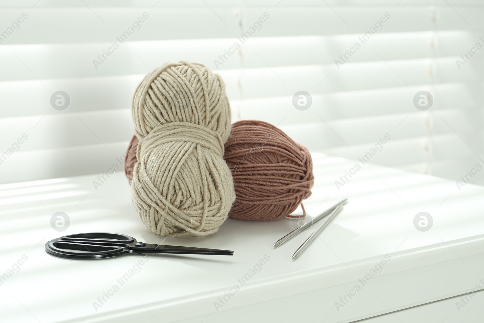 Photo of Soft yarn, knitting needles and scissors on chest of drawers indoors