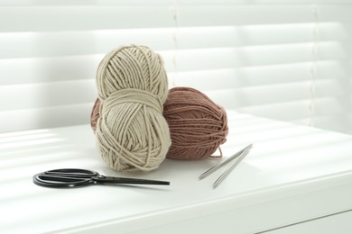 Photo of Soft yarn, knitting needles and scissors on chest of drawers indoors