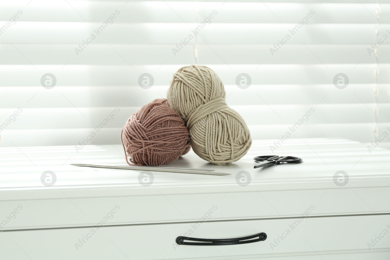 Photo of Soft yarn, knitting needles and scissors on chest of drawers indoors