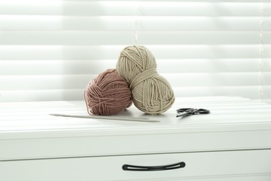 Photo of Soft yarn, knitting needles and scissors on chest of drawers indoors