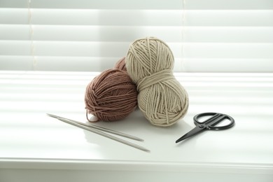 Photo of Skeins of soft yarn, knitting needles and scissors on white table indoors