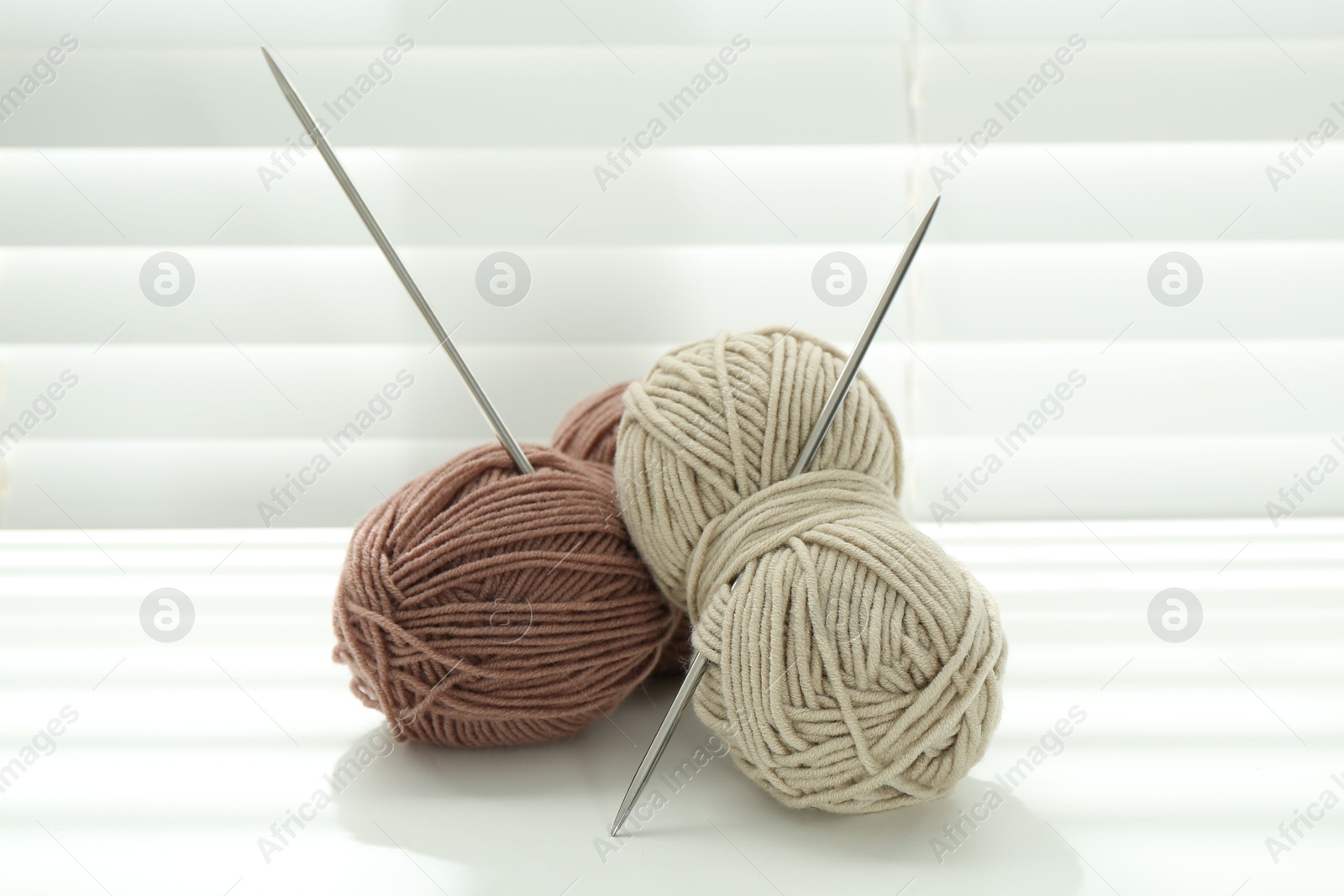 Photo of Skeins of soft yarn and knitting needles on white table indoors