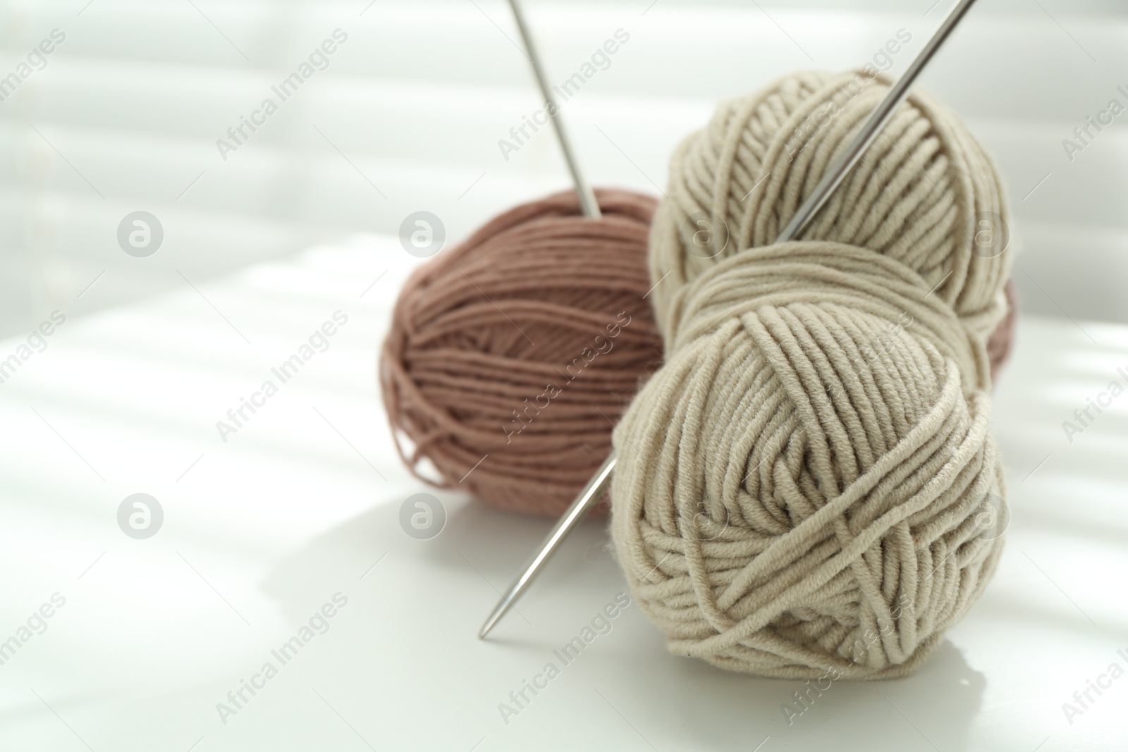 Photo of Skeins of soft yarn and knitting needles on white table indoors, closeup. Space for text