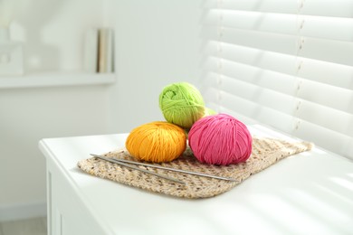 Photo of Skeins of soft yarn and knitting needles on white table indoors