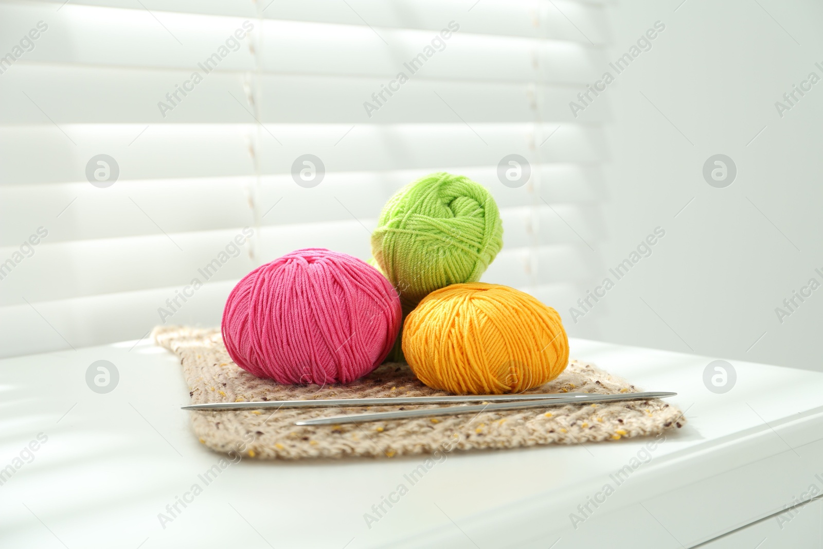 Photo of Skeins of soft yarn and knitting needles on white table indoors