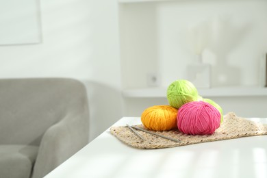 Photo of Skeins of soft yarn and knitting needles on white table indoors, space for text