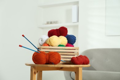 Photo of Skeins of soft yarn in crate and knitting needles on wooden table indoors