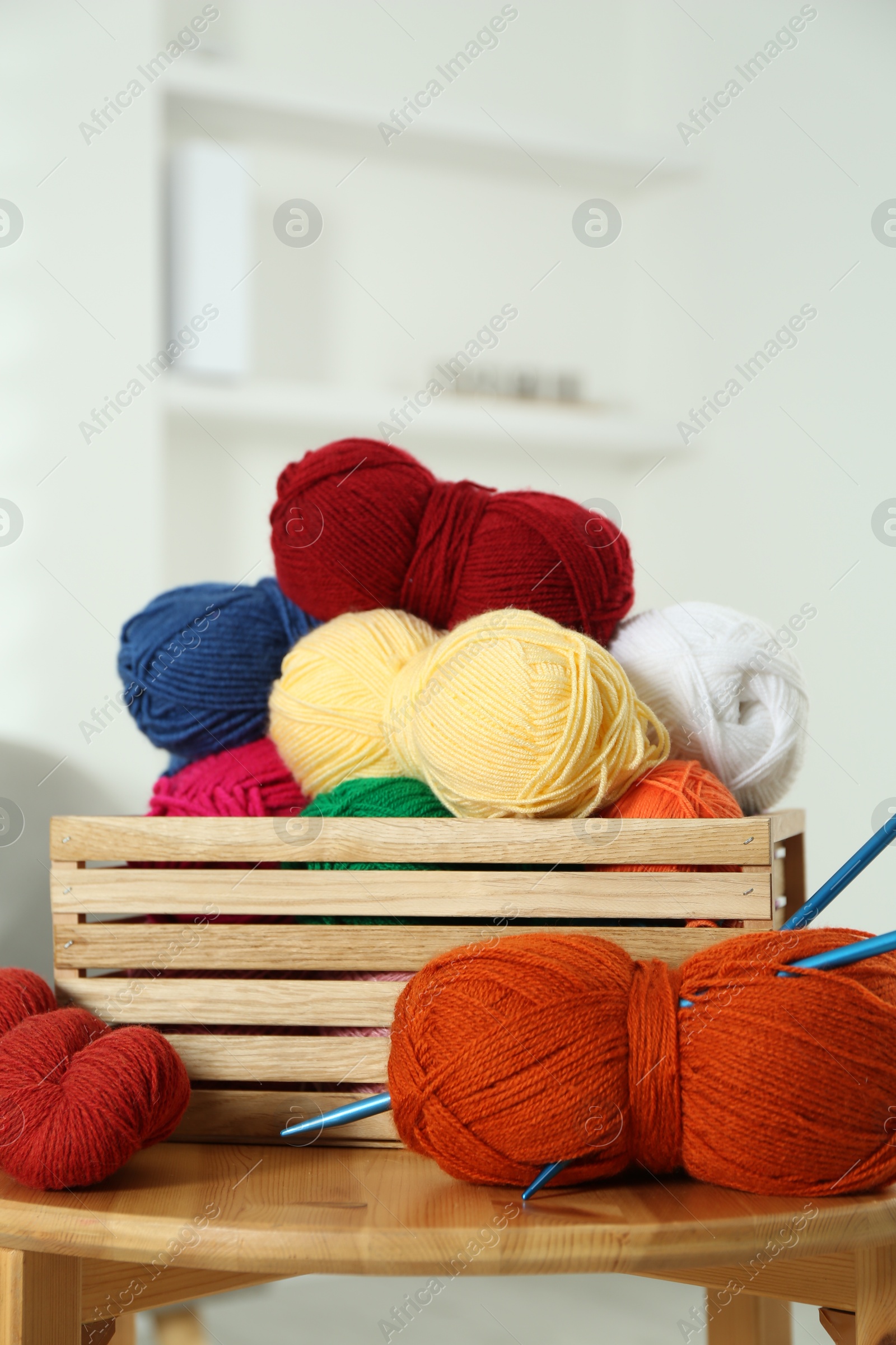 Photo of Skeins of soft yarn in crate and knitting needles on wooden table indoors