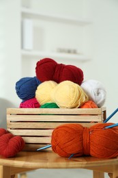 Skeins of soft yarn in crate and knitting needles on wooden table indoors