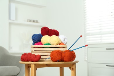 Skeins of soft yarn in crate and knitting needles on wooden table indoors