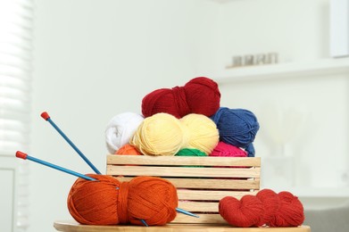 Skeins of soft yarn in crate and knitting needles on wooden table indoors