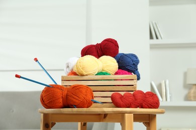 Photo of Skeins of soft yarn in crate and knitting needles on wooden table indoors