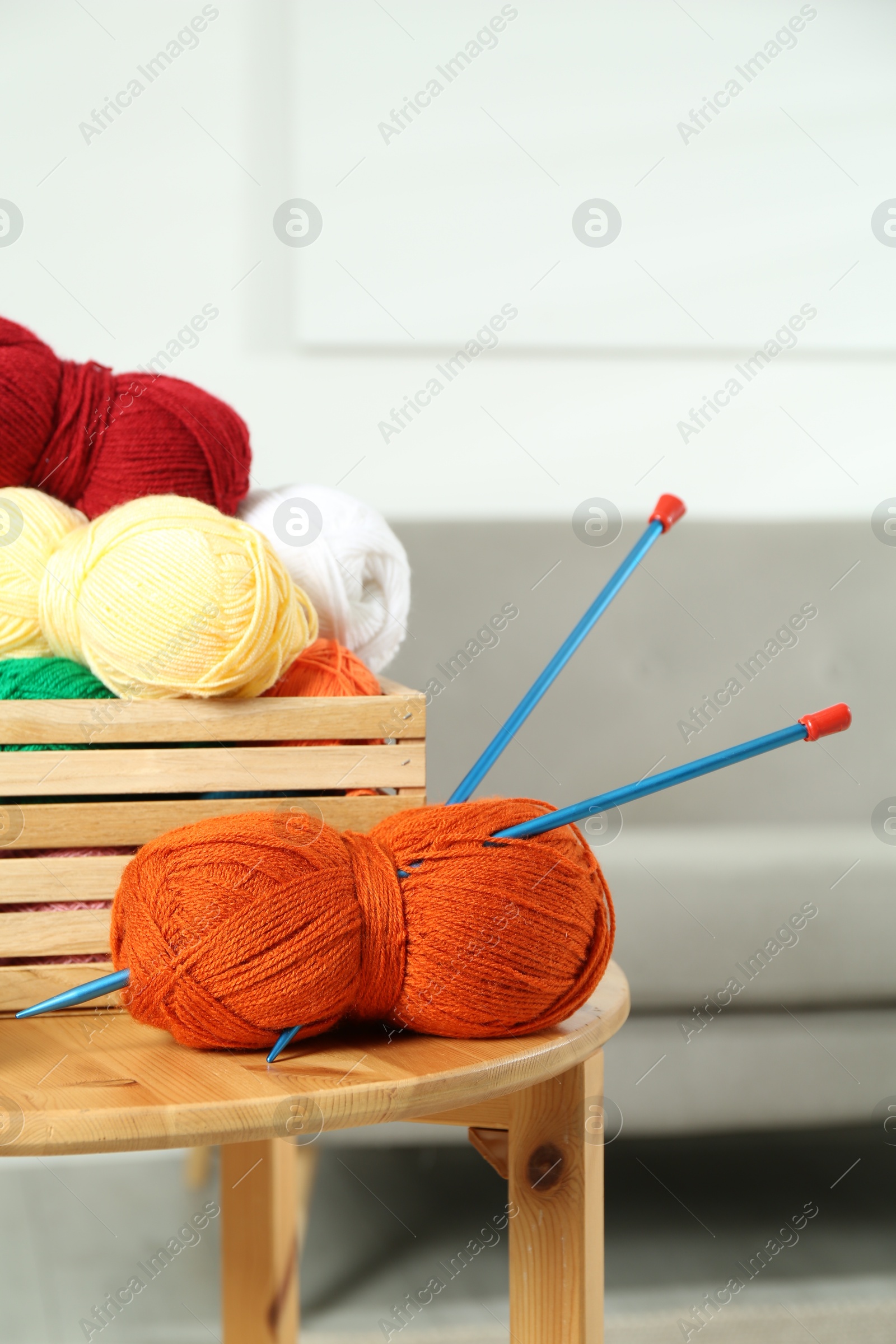 Photo of Skeins of soft yarn in crate and knitting needles on wooden table indoors