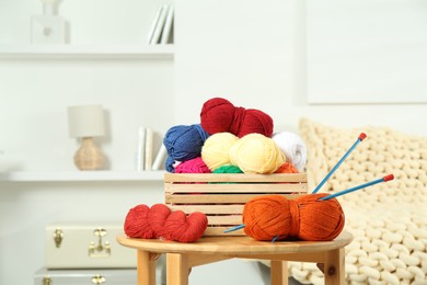 Skeins of soft yarn in crate and knitting needles on wooden table indoors