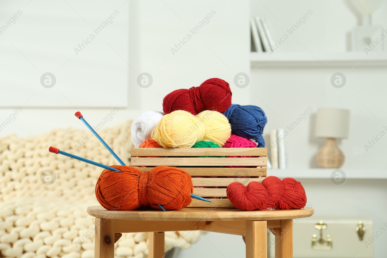 Photo of Skeins of soft yarn in crate and knitting needles on wooden table indoors