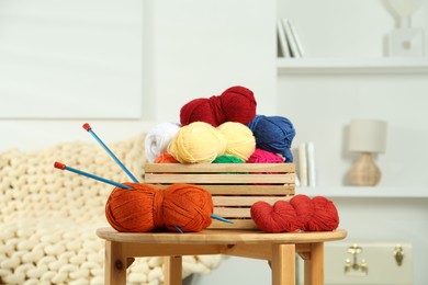 Skeins of soft yarn in crate and knitting needles on wooden table indoors