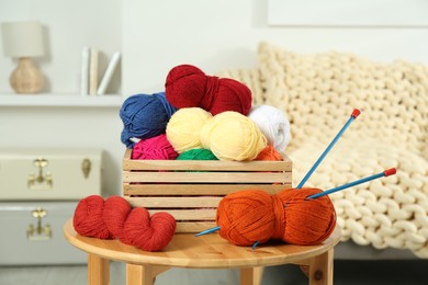 Photo of Skeins of soft yarn in crate and knitting needles on wooden table indoors