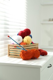 Photo of Soft yarn in crate and knitting needles on chest of drawers indoors