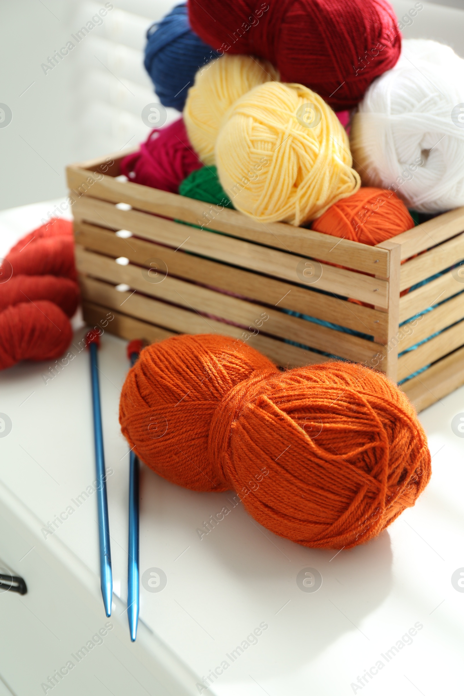 Photo of Soft yarn in crate and knitting needles on chest of drawers indoors, closeup