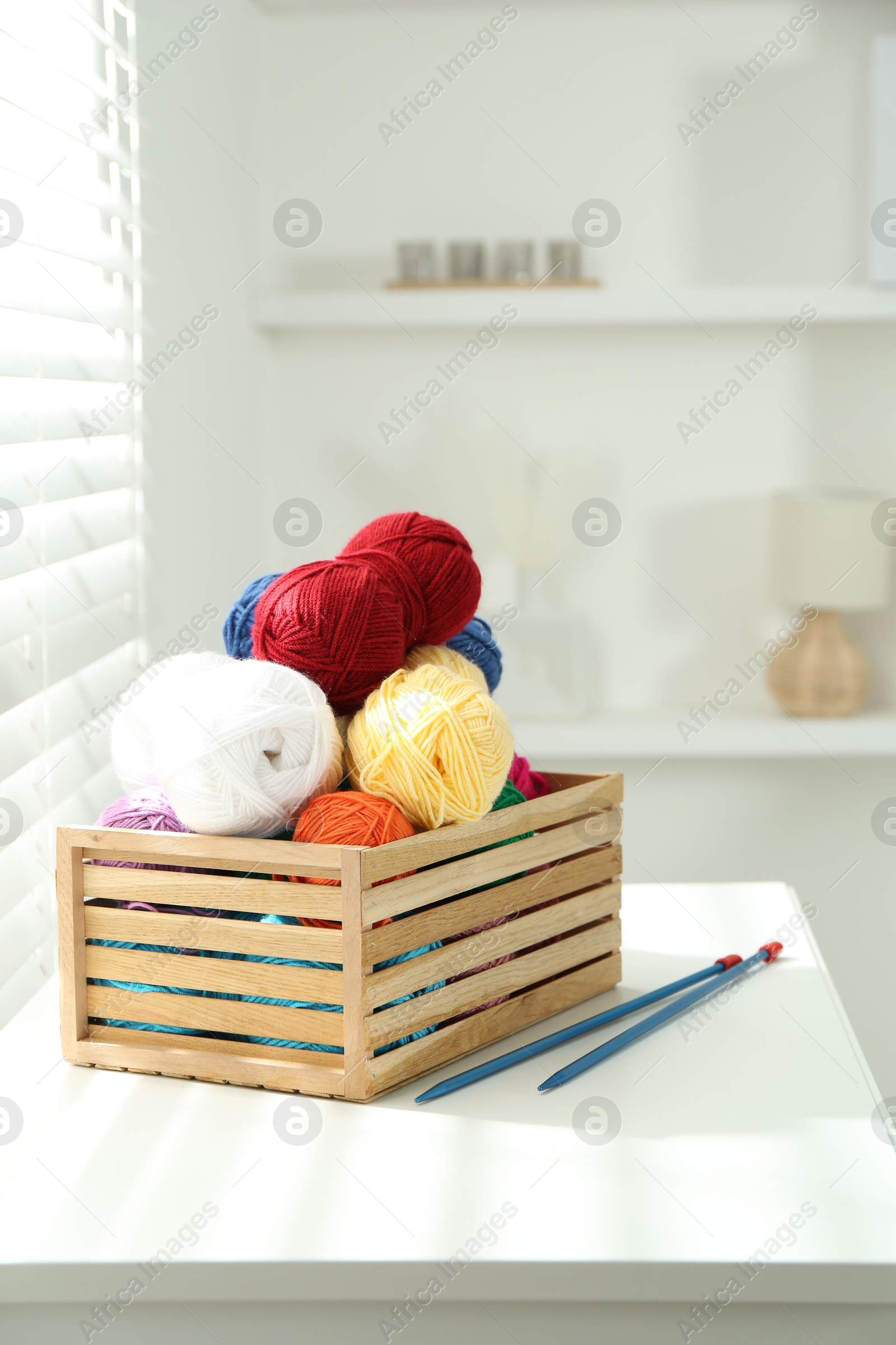 Photo of Skeins of soft yarn in crate and knitting needles on white table indoors