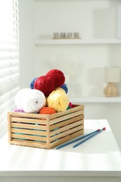 Photo of Skeins of soft yarn in crate and knitting needles on white table indoors